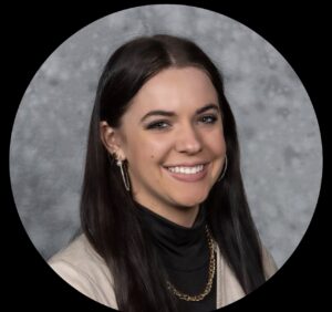 A woman with long dark hair, wearing a black top, beige jacket, gold hoop earrings, and a gold chain necklace, smiles in front of a gray mottled background—reflecting the spirit of a pro-life safety net.
