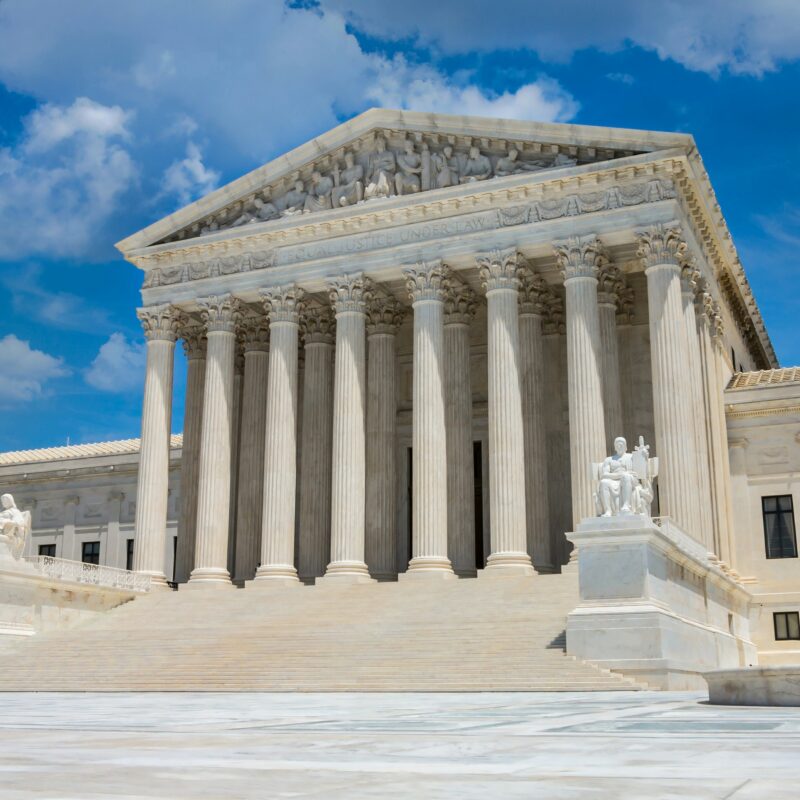 The United States Supreme Court building in Washington, D.C., featuring large columns and marble steps under a blue sky with clouds, stands as a symbol of justice and serves as a foundation for the nation’s pro-life safety net. Statues flank the entrance.