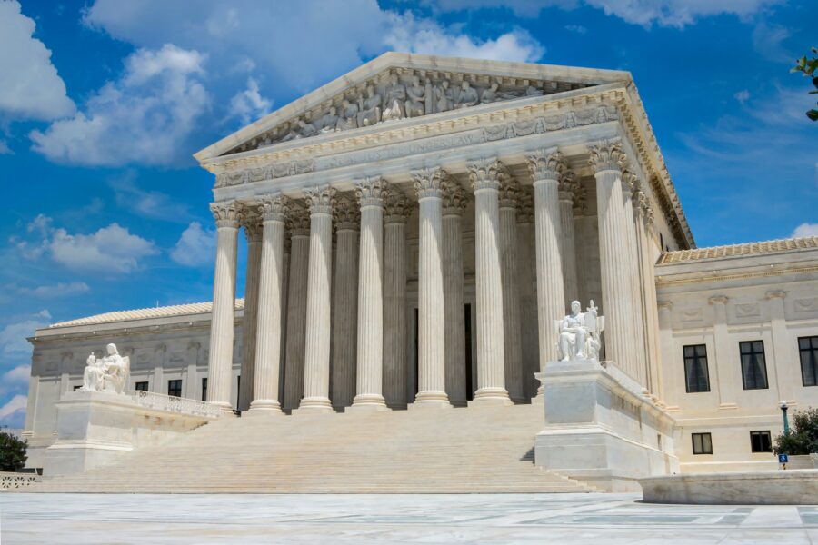 The United States Supreme Court building in Washington, D.C., featuring large columns and marble steps under a blue sky with clouds, stands as a symbol of justice and serves as a foundation for the nation’s pro-life safety net. Statues flank the entrance.