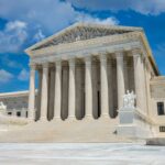 The United States Supreme Court building in Washington, D.C., featuring a large staircase, tall columns, statues, and intricate architectural details under a bright blue sky with scattered clouds.